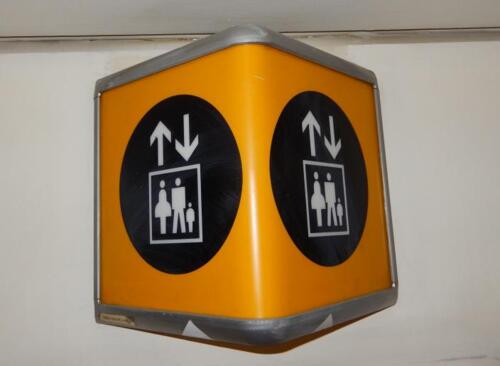 Wall mounted illuminated elevator sign. Curved metal box construction in a triangle form.